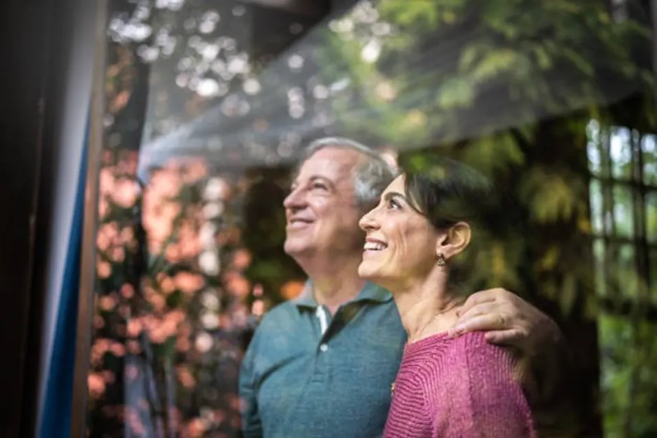 Happy mature couple smiling and looking upward together through a window surrounded by greenery