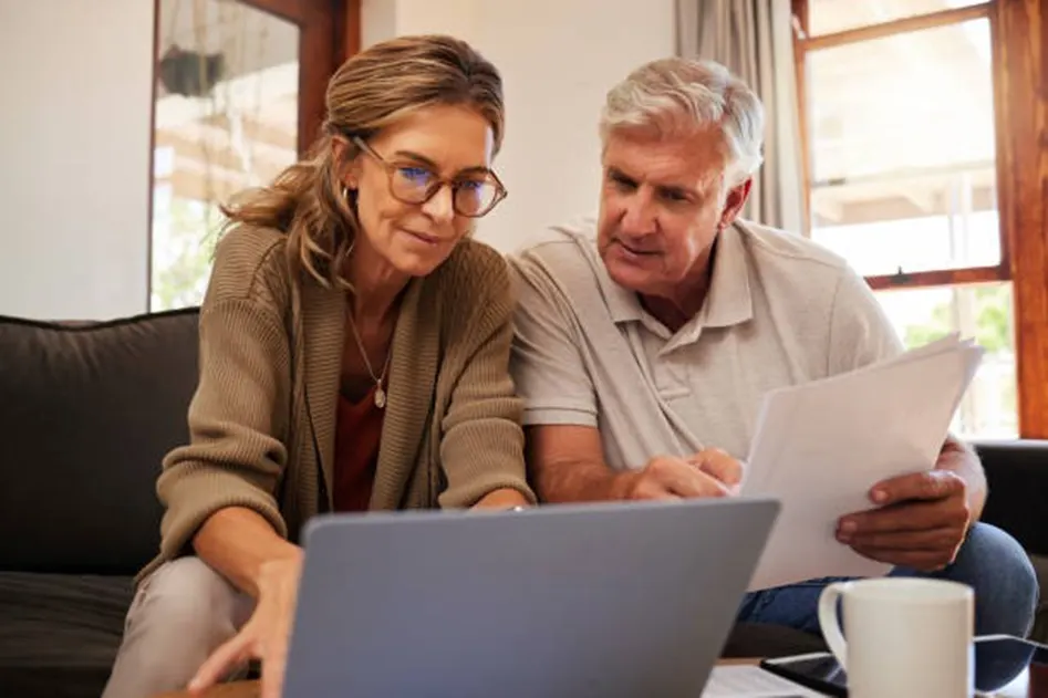 Mature couple sitting on a sofa reviewing a document together beside a laptop
