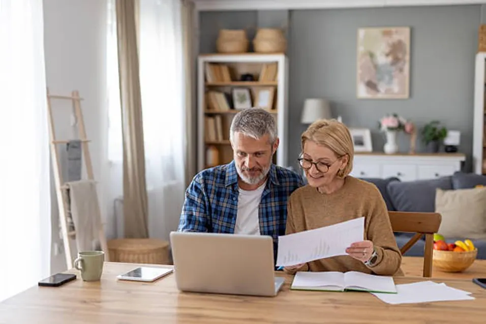 Mature couple smiling and reviewing documents together at a laptop at home
