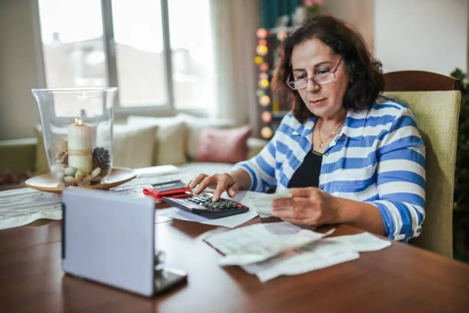 Middle-aged woman using a calculator and reading receipts at a dining table