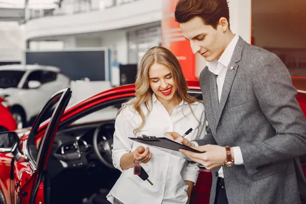 Couple signing auto loan paperwork beside a new car