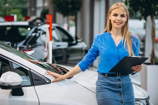 Saleswoman with a clipboard standing beside a car in a showroom