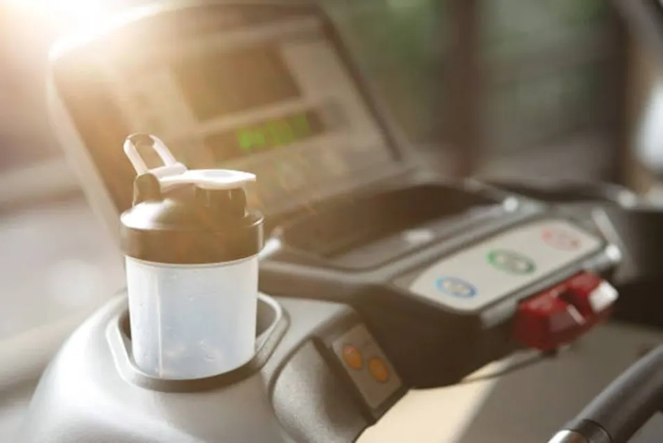 Protein shaker bottle on a treadmill in a sunlit gym