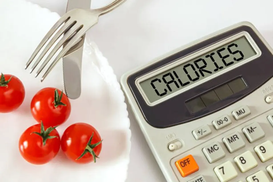 Calculator displaying CALORIES beside cherry tomatoes and cutlery on a plate