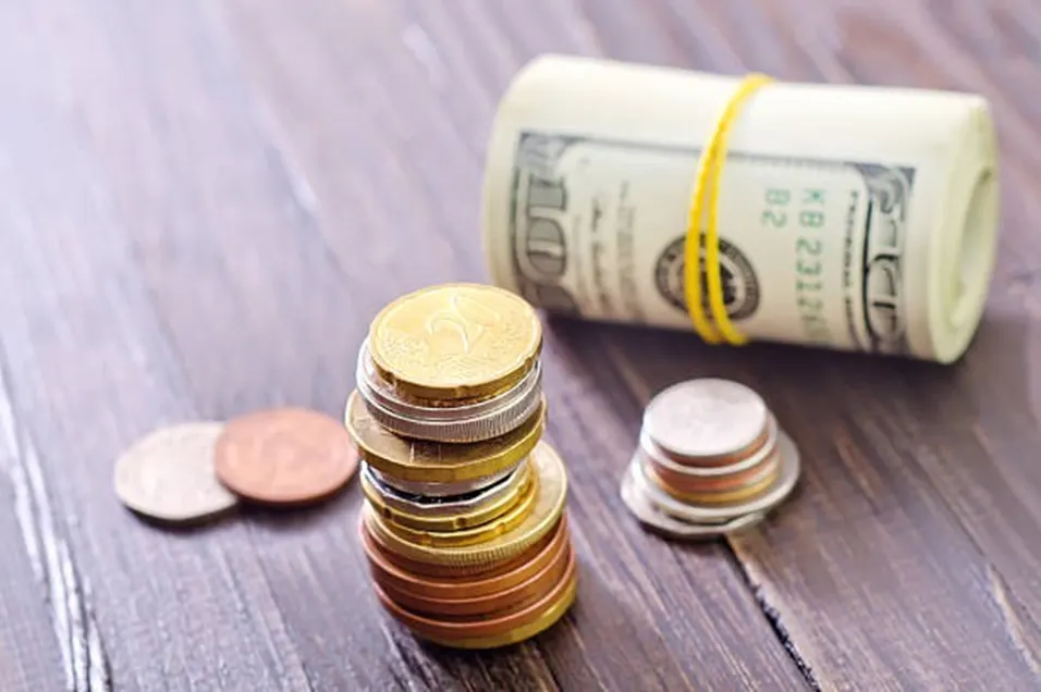 Stack of coins and a rolled dollar bill on a wooden surface