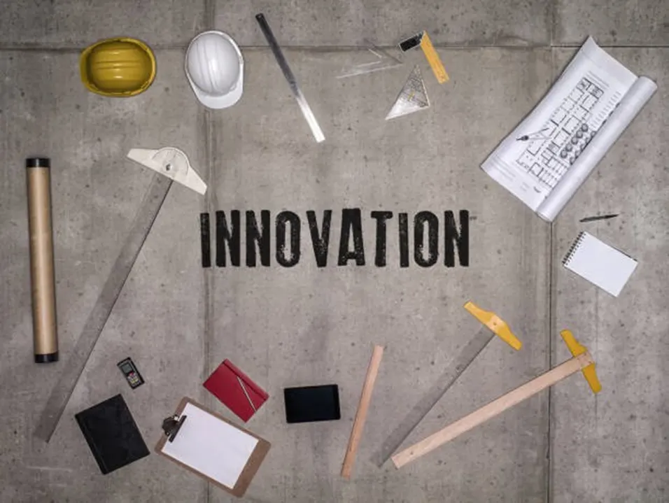 Flat lay of construction tools, hard hats, blueprints and ruler on a concrete surface with the word INNOVATION