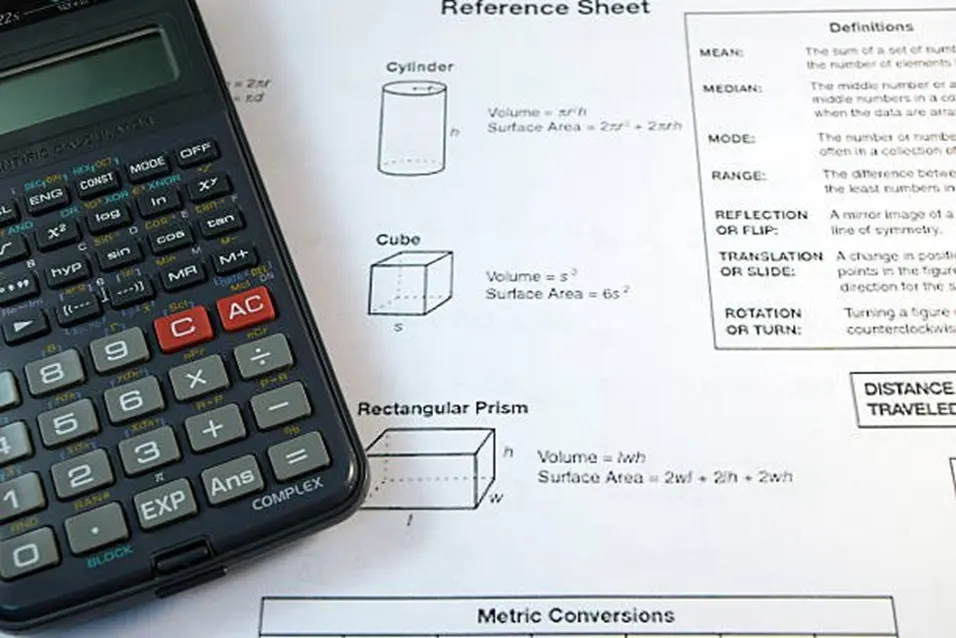 Scientific calculator resting on a math reference sheet showing metric conversions and geometry formulas