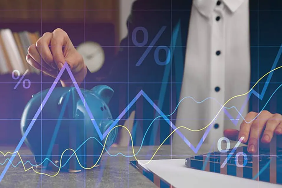 Person inserting coin into a blue piggy bank beside a calculator with financial charts and percent signs overlaid