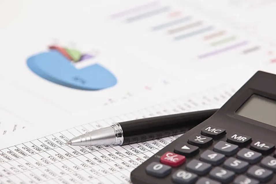 Black calculator and pen resting on financial charts with a pie chart and bar graph in the background
