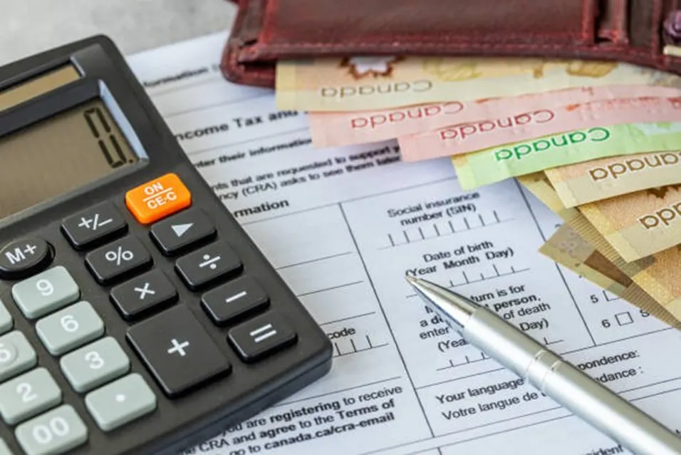 Black calculator beside Canadian banknotes, a leather wallet and a silver pen on an income tax form