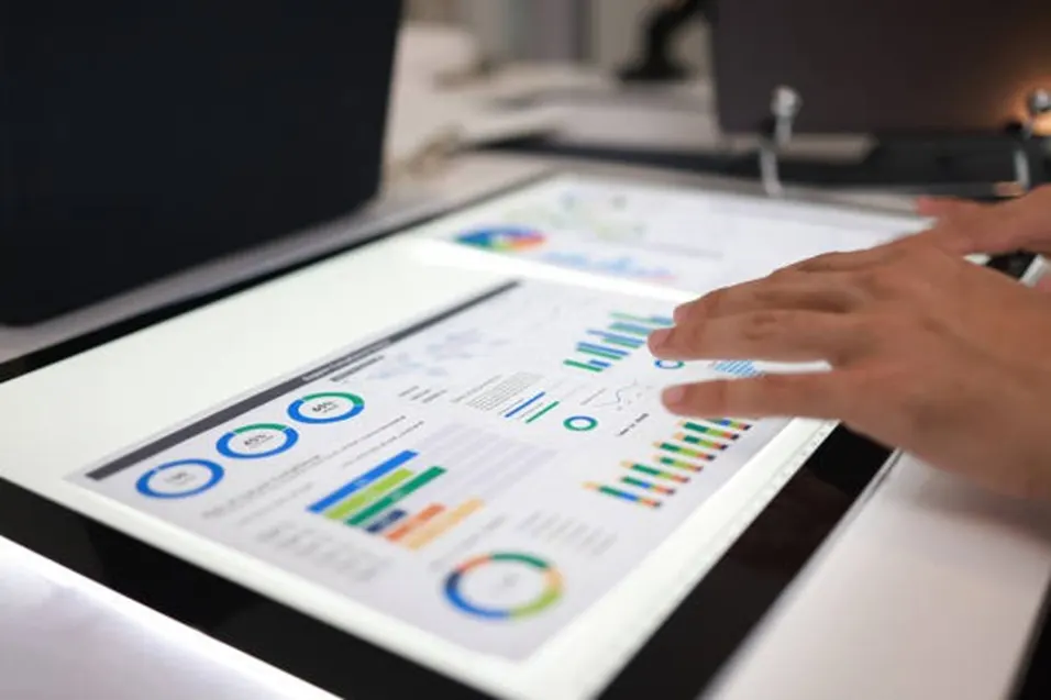 Person pointing at colourful charts and graphs on a large touchscreen display