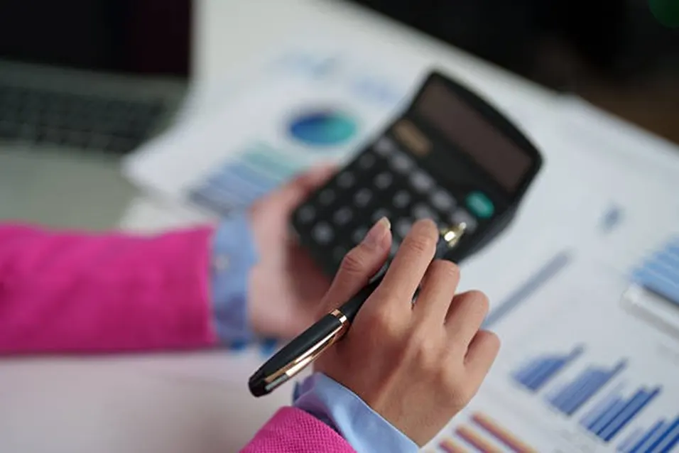 Woman in pink jacket holding a calculator and pen over financial charts and bar graphs