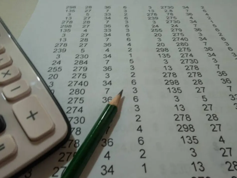 Calculator and green pencil resting on a sheet filled with rows of numbers