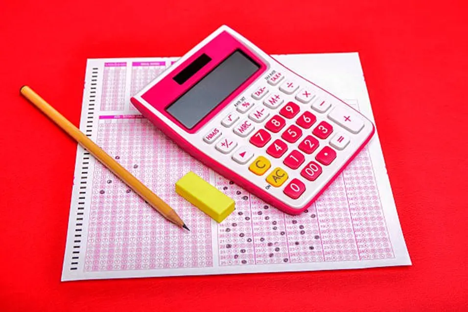 Pink calculator and pencil resting on a multiple-choice answer sheet on a red background