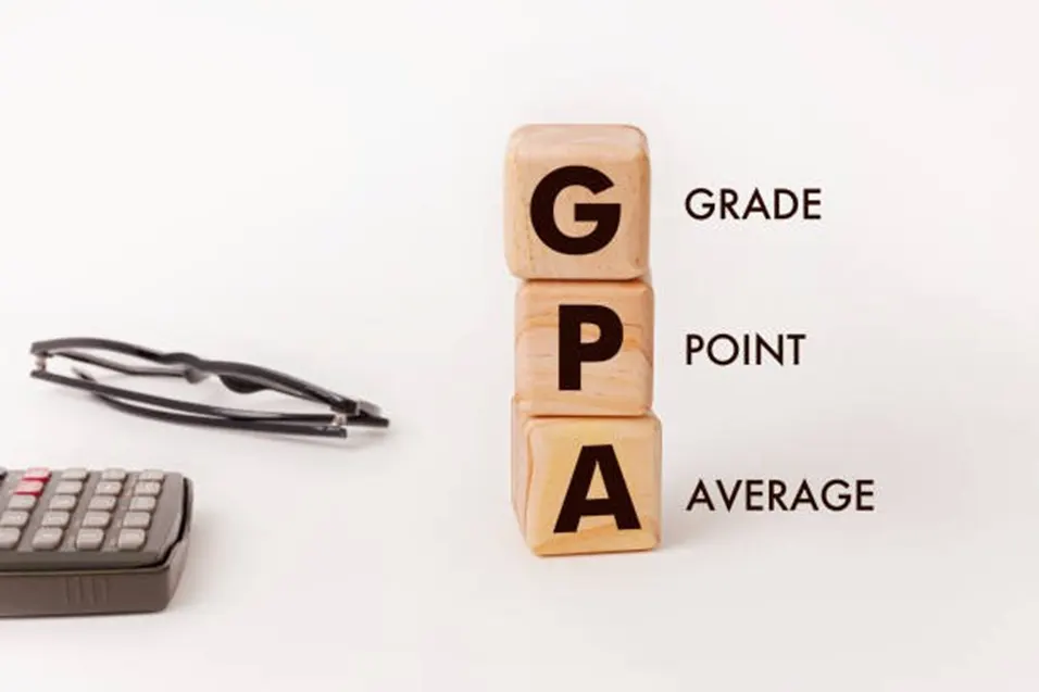 Wooden blocks spelling GPA beside glasses and a calculator on a white surface