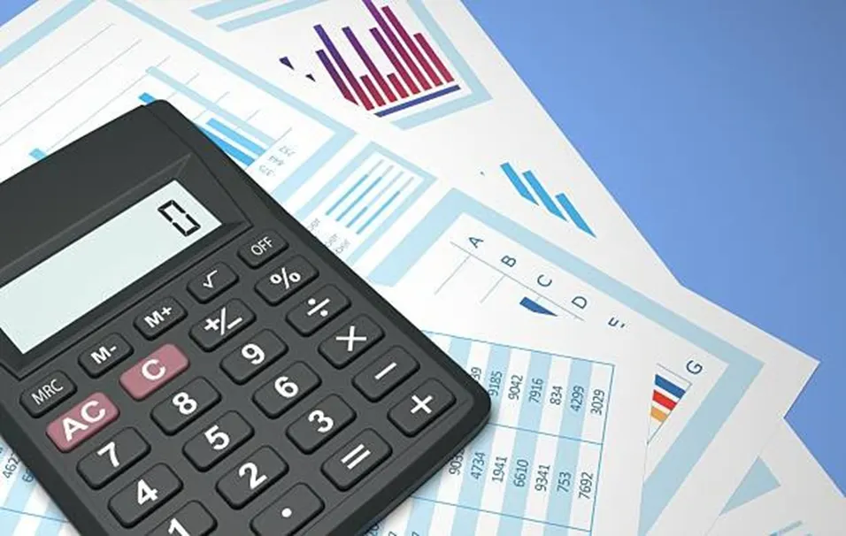 Black calculator resting on printed reports showing bar charts, pie charts, and data tables on a blue background
