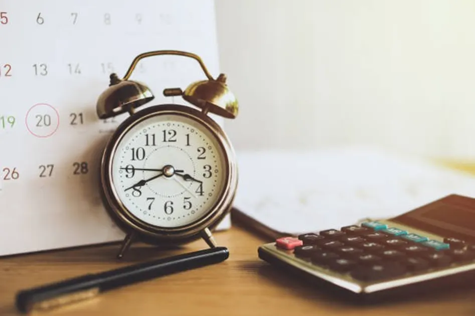 Vintage alarm clock beside a pen and calculator in front of a wall calendar with circled dates