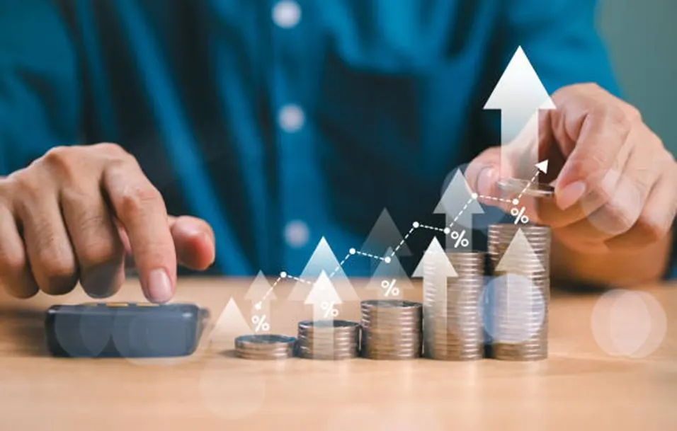 Person using a calculator beside growing stacks of coins with glowing percentage and upward arrow overlays