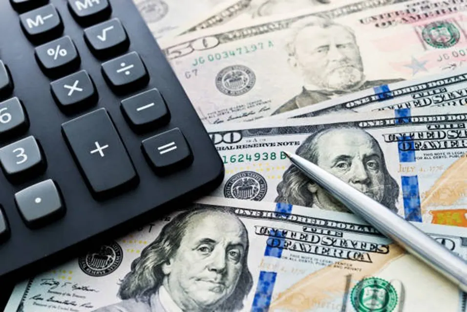 Calculator placed on top of US dollar bills with a pen symbolising investment returns