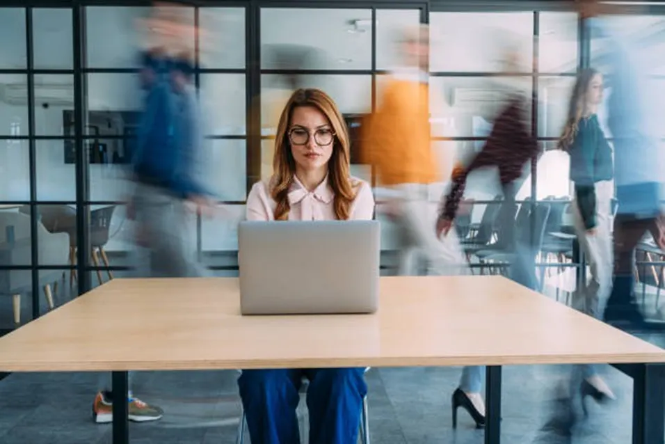 Woman focused at laptop in a busy fast-paced office environment
