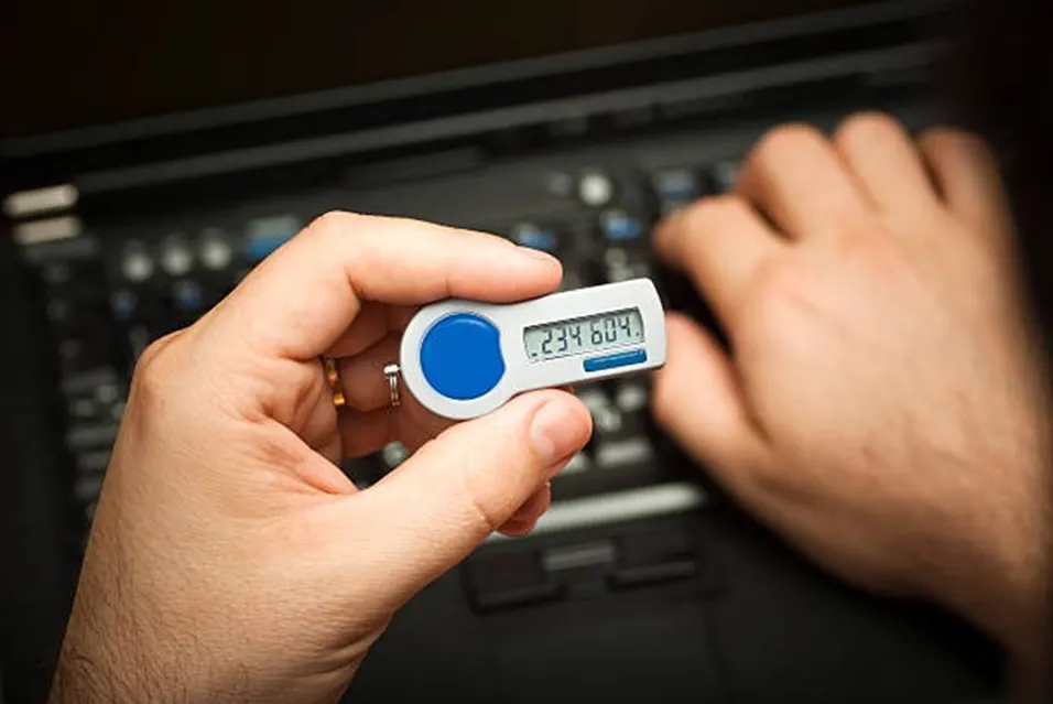 Person holding a hardware security token displaying a one-time code in front of a laptop keyboard