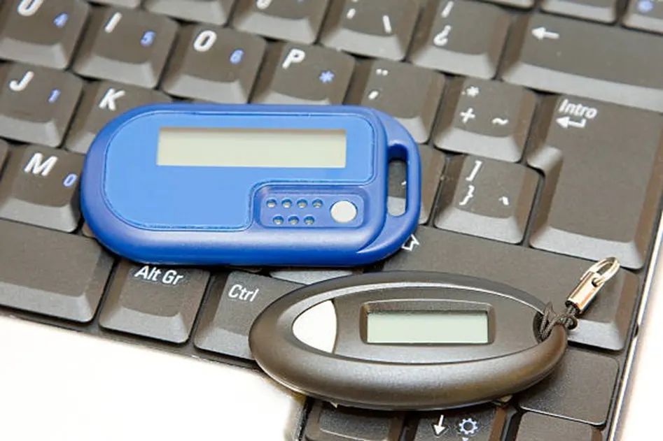 Two hardware security key fobs — one blue, one grey — resting on a laptop keyboard