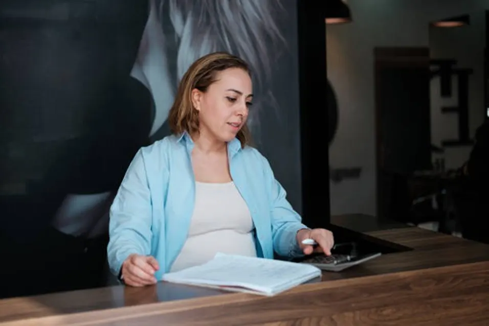 Pregnant woman using a calculator and reviewing documents at a reception desk
