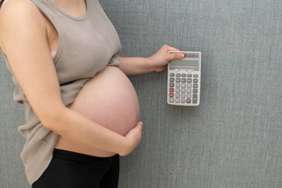 Pregnant woman holding a calculator against a textured wall