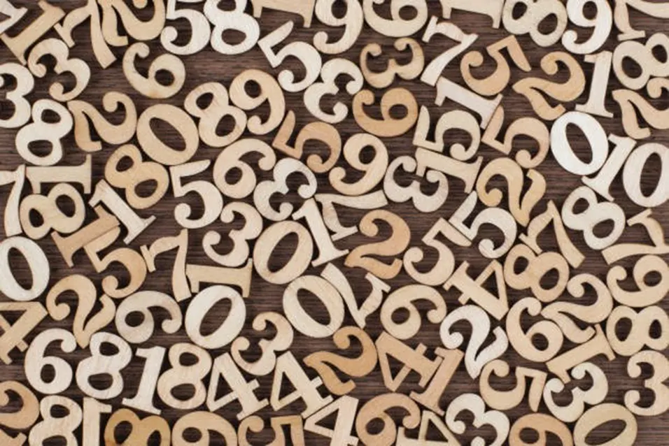 Scattered wooden number tiles from 0 to 9 spread randomly across a dark wooden surface