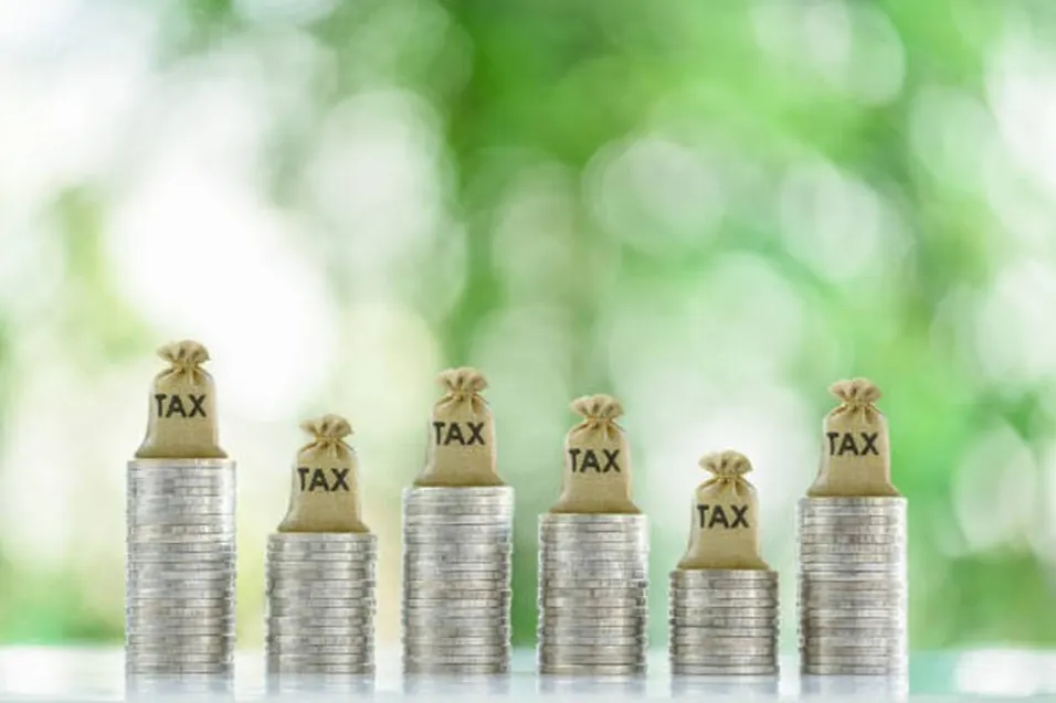 Six stacks of coins with tax bags on top arranged in varying heights against a green bokeh background