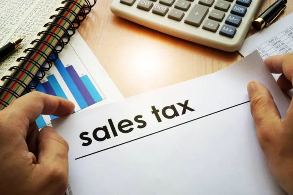 Hands holding a sales tax document with a calculator, notebook, and bar chart on a desk