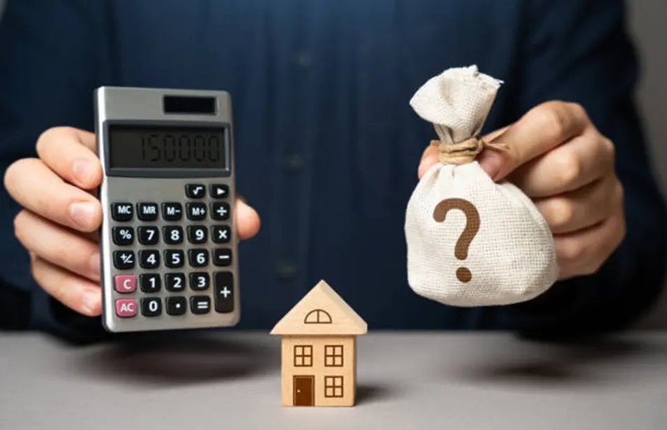 Person holding a calculator and a money bag with a question mark beside a small wooden house model