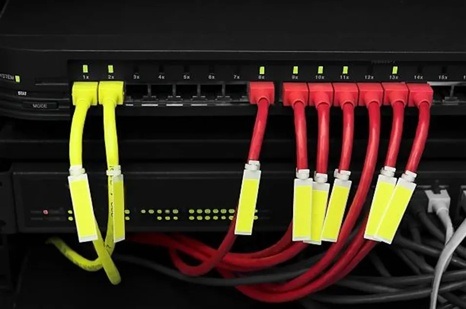 Yellow and red labelled ethernet cables connected to a black network switch in a server rack