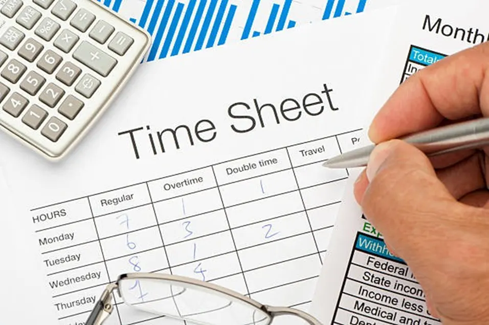 Time sheet form being filled in with a pen showing regular and overtime hours, alongside a calculator and monthly report