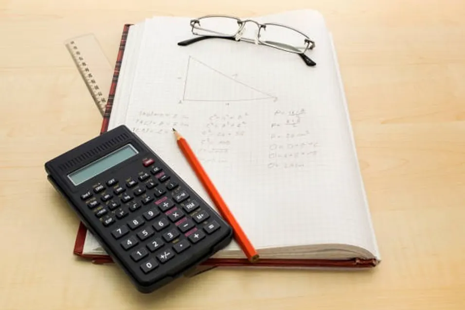 Scientific calculator and orange pencil on a notebook with a hand-drawn triangle and geometry calculations, glasses resting on top