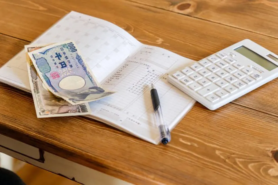 Open accounting ledger with banknotes, a pen, and a white calculator on a wooden desk