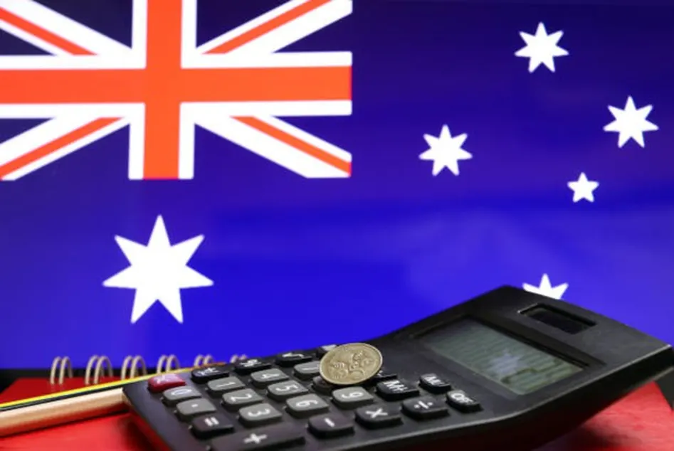 Black calculator with an Australian coin on top in front of the Australian flag with a red notebook