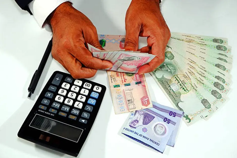 Hands sorting UAE dirham notes beside a black calculator and pen on a white surface
