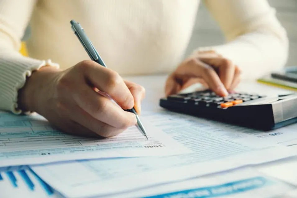 Person writing on a US 1040 tax form while using a calculator at a desk